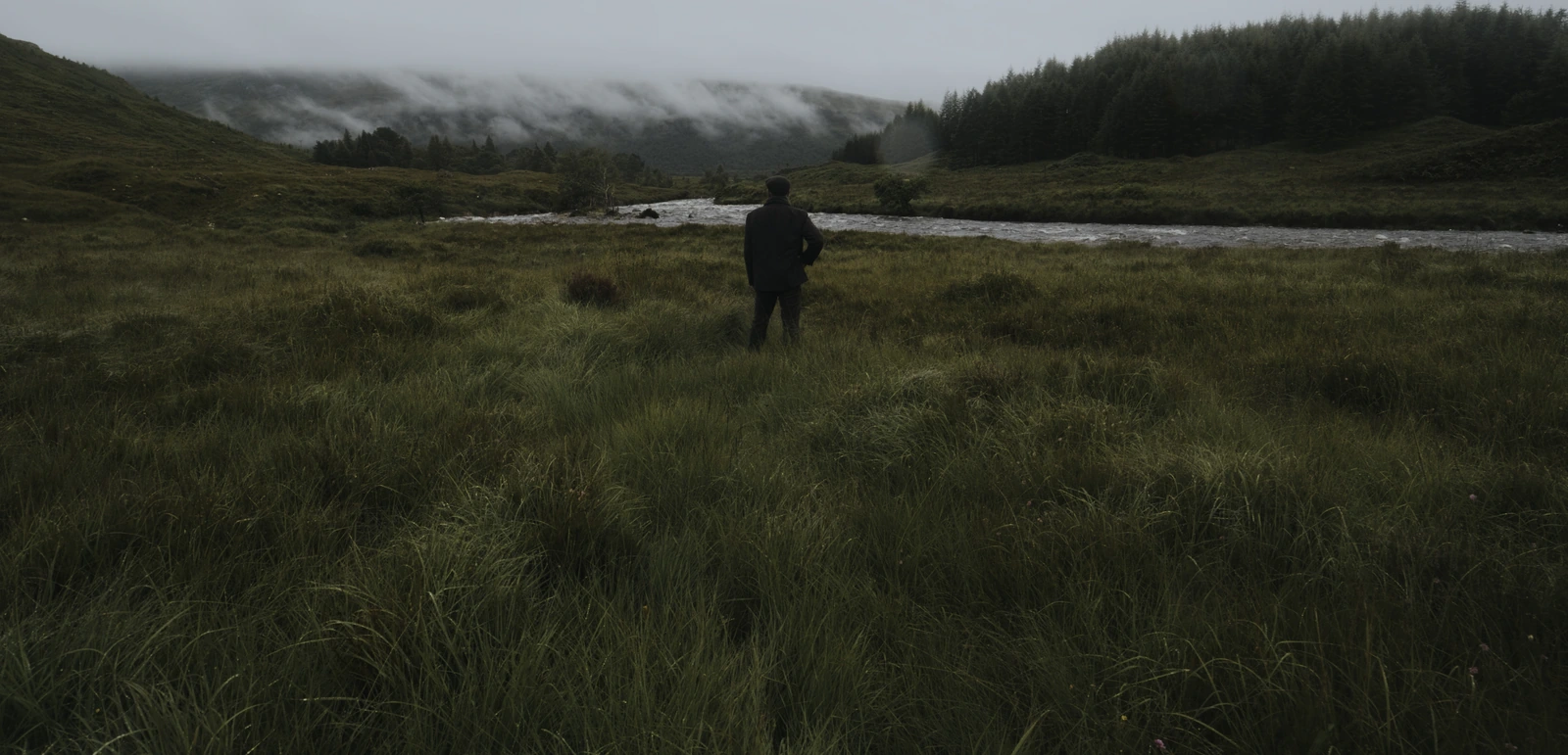 Person am Fluss in einer nebligen schottischen Landschaft