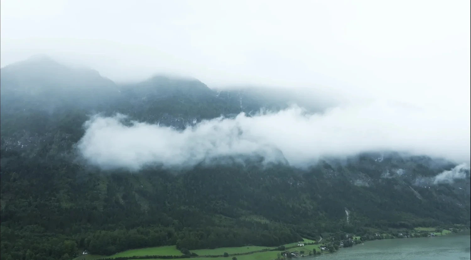 Wolken über einem bewaldeten Berghang am See