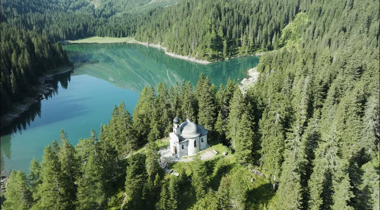 Luftbild: Kapelle über einem türkisfarbenen Bergsee